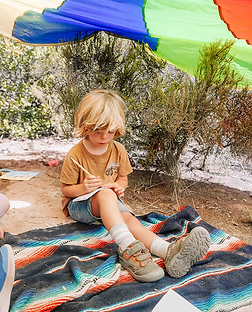 Preschool child participating in nature-based learning, journaling independently near a creek at forest school.