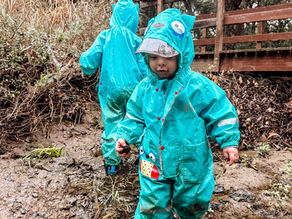 Two preschool children playing in a creek in the rain at a nature preschool, building resilience and joy through all-weather outdoor exploration.