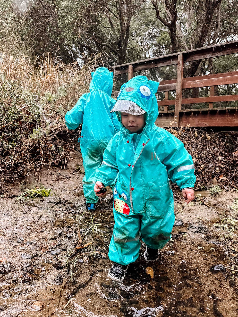 Two preschool children playing in a creek in the rain at a nature preschool, building resilience and joy through all-weather outdoor exploration.