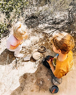 Young children engaged in child-led exploration and nature journaling on a rock during forest school.